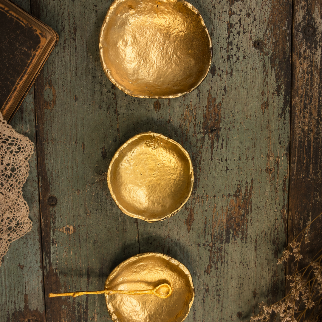 Overhead view of three hammered gold dishes and one spoon