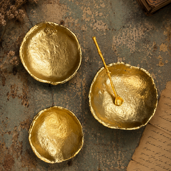 Three gold condiment dishes with a spoon resting in one dish