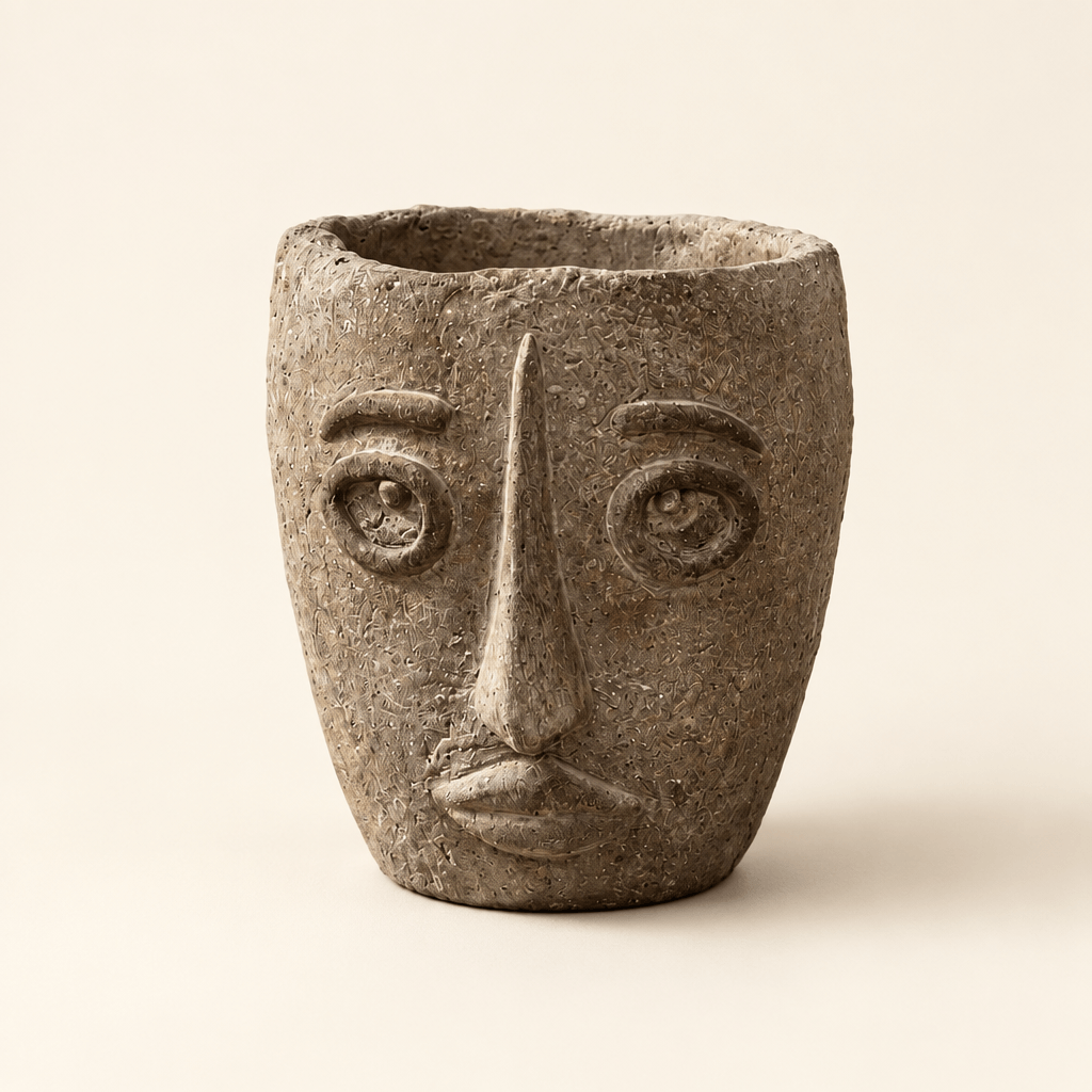 Earthy brown-gray cement face planter with raised eyes, a long nose, and sculpted lips on an ivory background