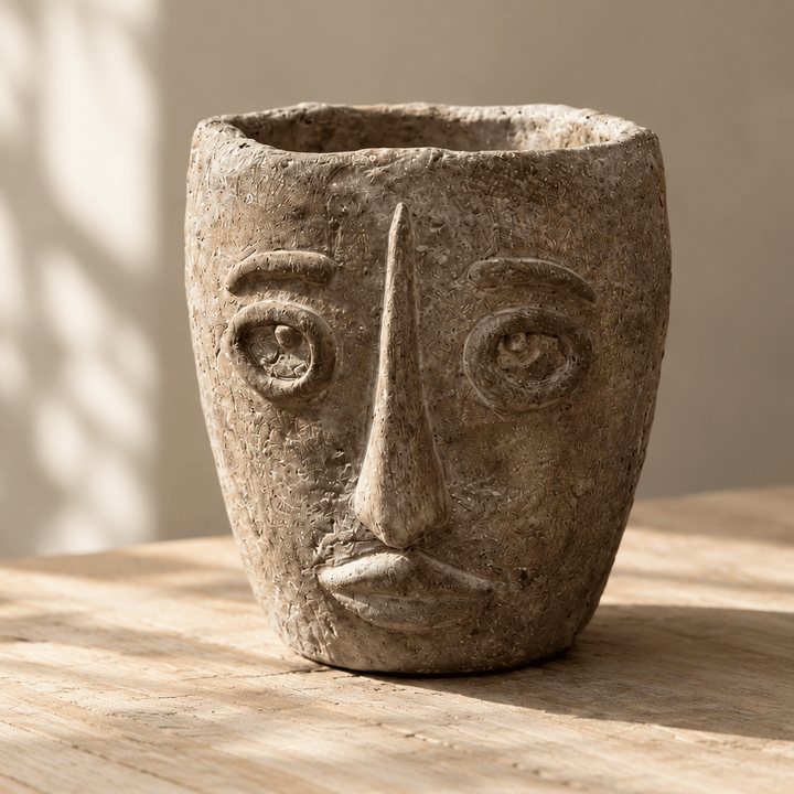 Detail of raised facial features, an irregular rim, and rough earthy texture on a cement face planter