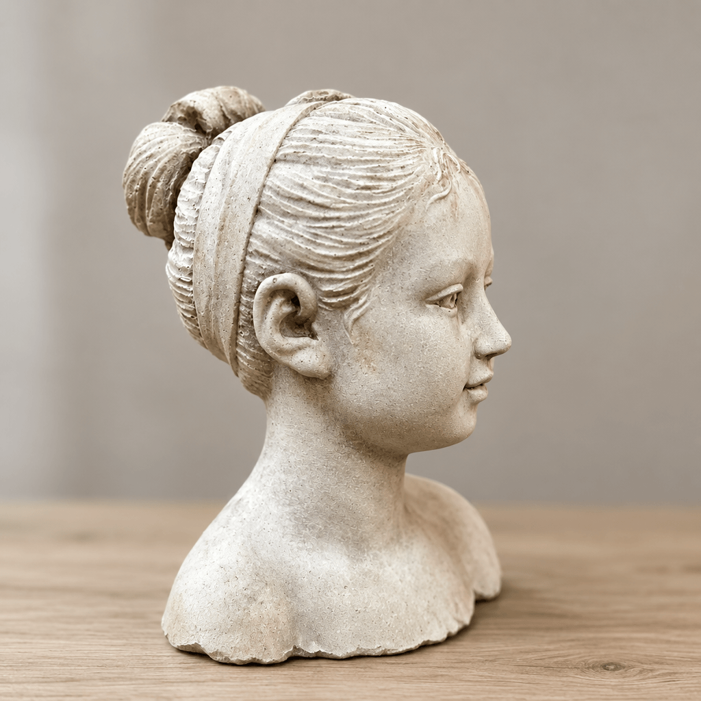 Profile detail of a cement girl bust showing sculpted facial features, carved hair ribbon, and bun