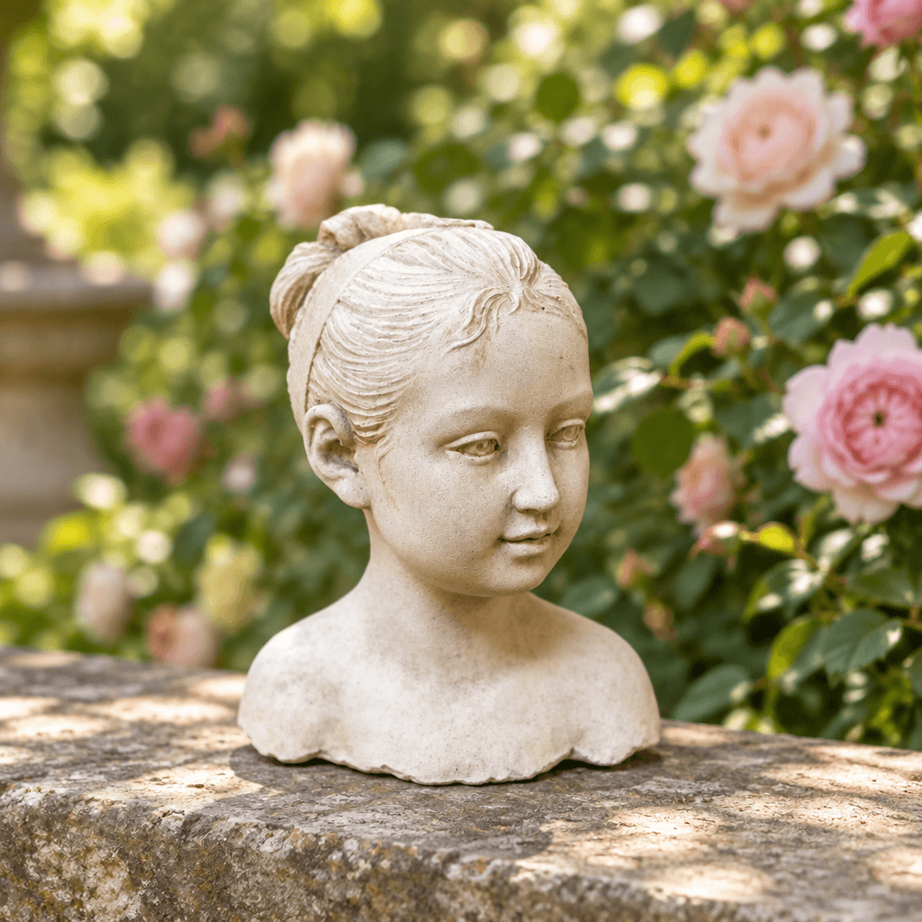 Hand-cast cement girl bust on a weathered stone garden ledge with greenery and roses behind