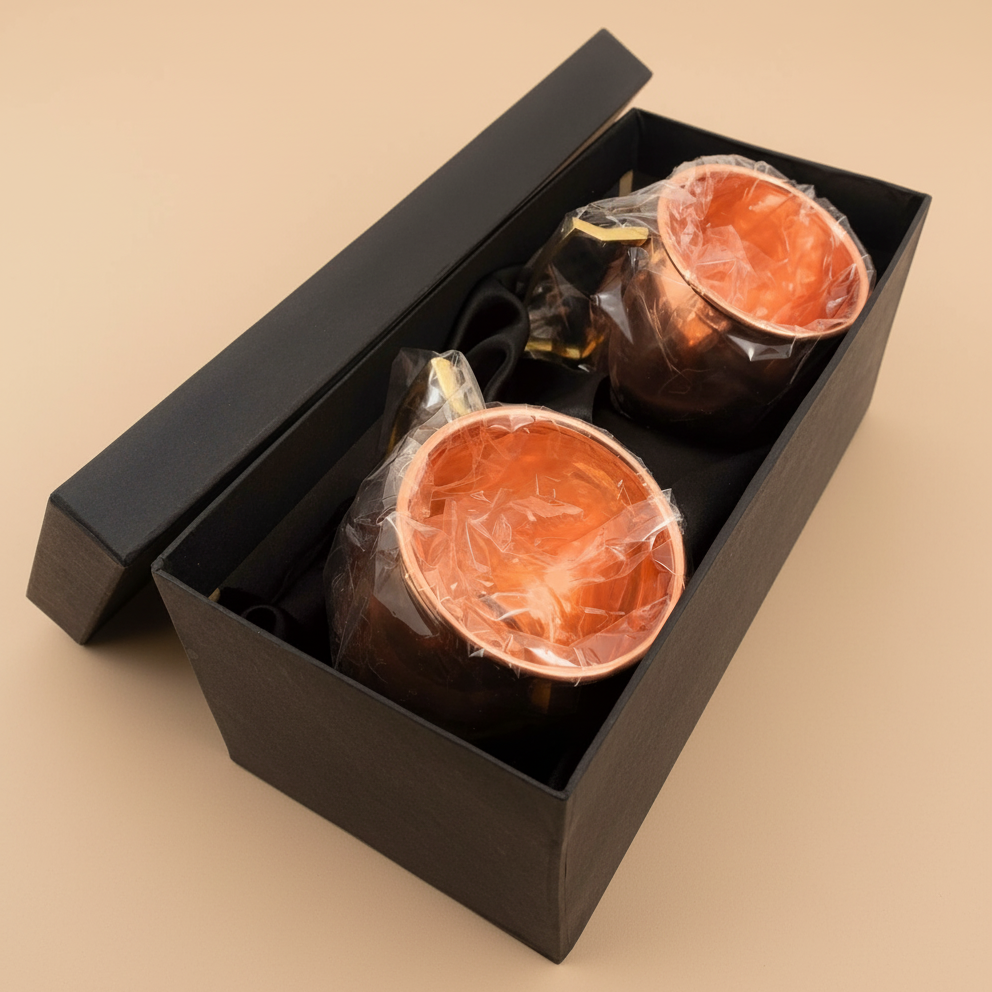 Two copper mugs in a black box on a beige background