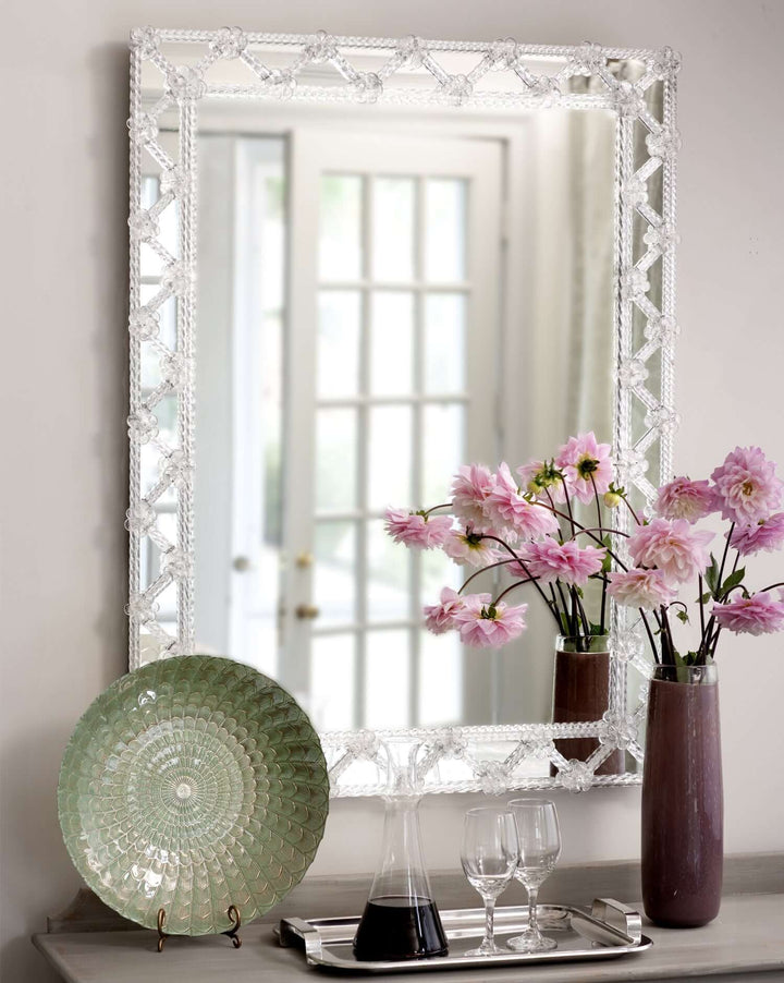 Handcrafted Murano Glass Mirror with Clear Rosettes displayed on a wall reflecting a room with floral decor and a decorative plate