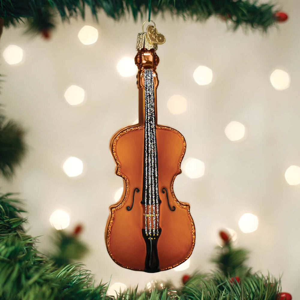 Handcrafted Glass Cello Christmas Ornament hanging on a festive tree branch with blurred holiday lights in the background.