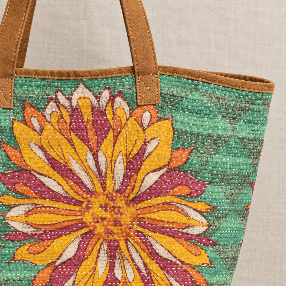 Close view of a tan leather handle attachment and kantha stitching on green floral cotton fabric