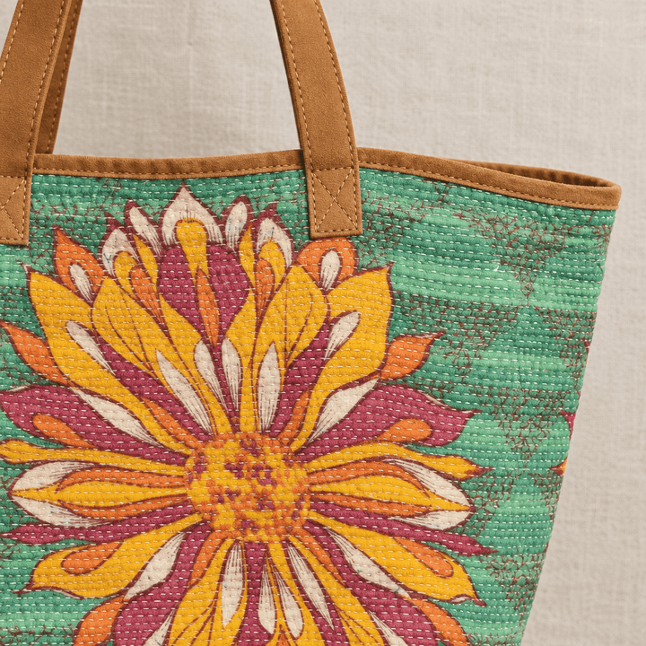 Close view of a tan leather handle attachment and kantha stitching on green floral cotton fabric