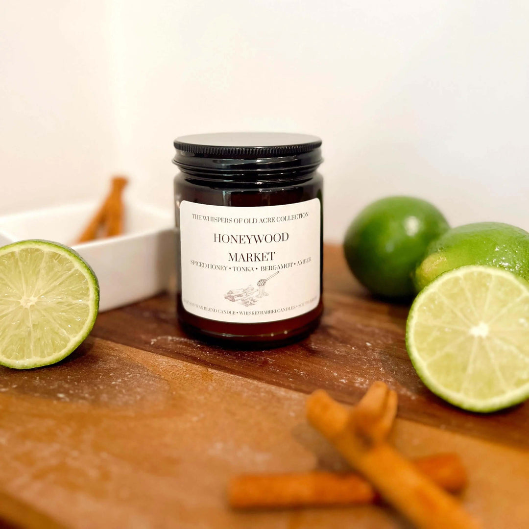 Honeywood Market Scented Candle: Spiced Honey, Tonka & Amber with lime and cinnamon sticks on rustic table.