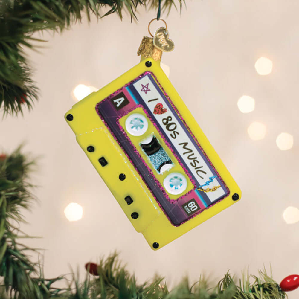 I Love the 80s Cassette Tape Christmas Ornament hanging on a tree, featuring a retro yellow cassette design with '80s Music' label.