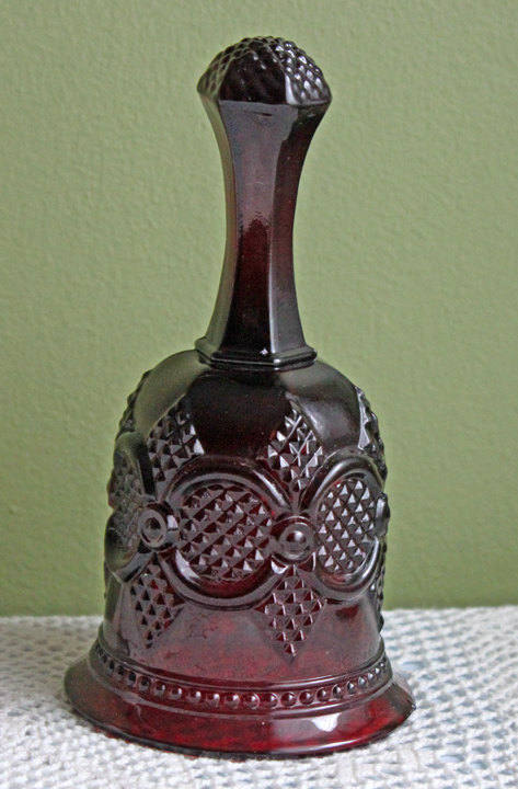 Glass Bell by Avon - Cape Cod Collection Ruby Color Sandwich Glass displayed against a green background.