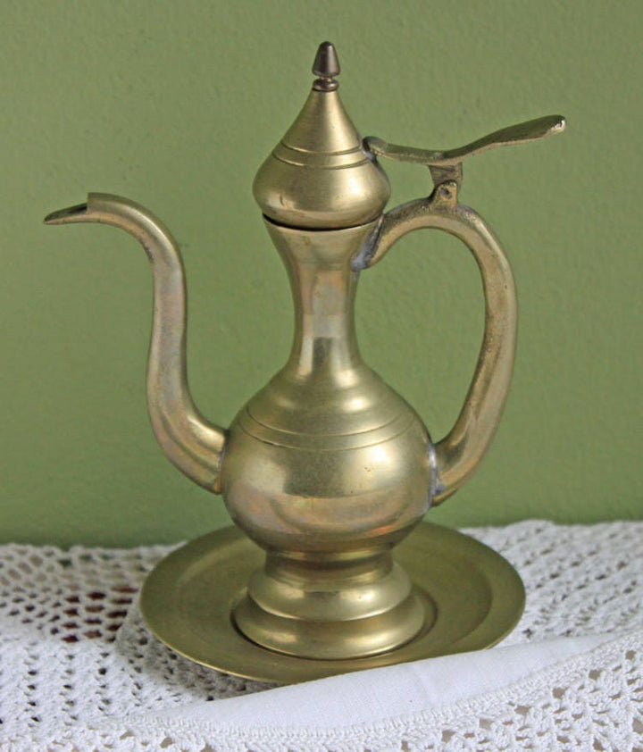 Vintage Brass Pitcher with Hinged Lid and Plate displayed on a doily against a green background.