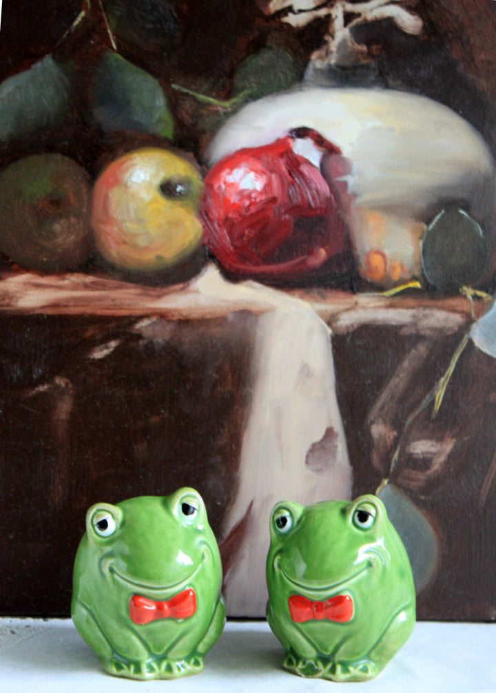 Salt and Pepper Whimsical Frog Shakers with Red Bow Ties in front of a fruit still life painting.