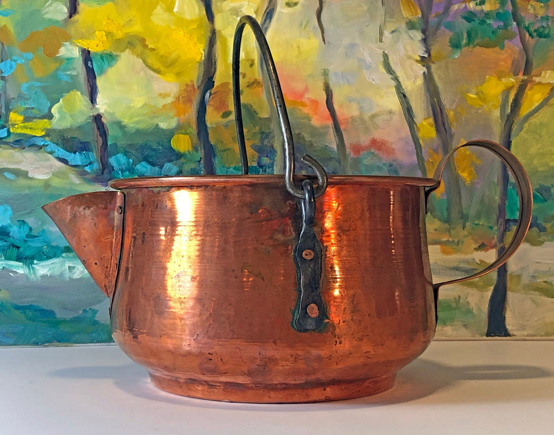Antique copper kettle with a handle on a colorful painted background. Perfect rustic kitchen decor.