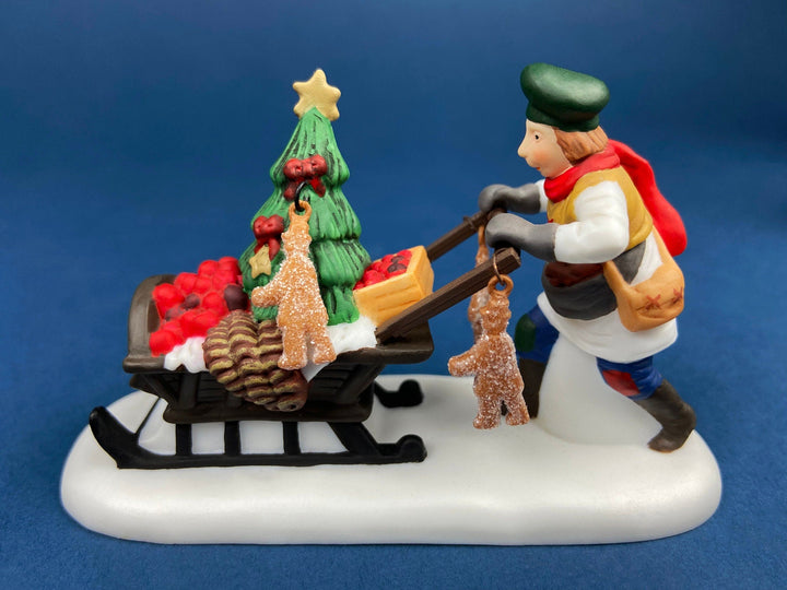Department 56 Dickens Village Gingerbread Vendor with Kids figurine carrying a Christmas tree and treats.