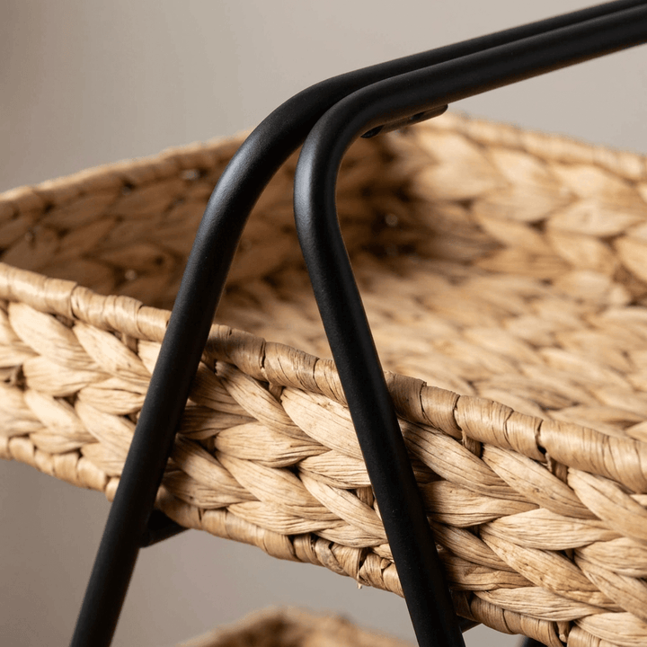 Close-up of the Seraphine Two-Tier Basket Stand showing the braided hyacinth basket texture where the black iron frame meets the basket rim