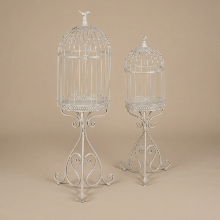 Two soft-white iron birdcage planters with domed tops, songbird finials, and scrollwork pedestal legs.