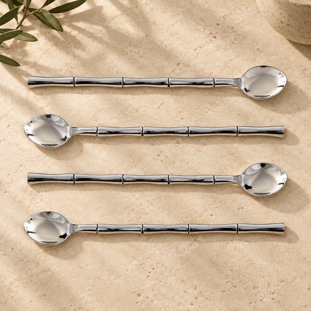 Four silver stainless steel stirring spoons with bamboo-style handles arranged on ivory limestone.