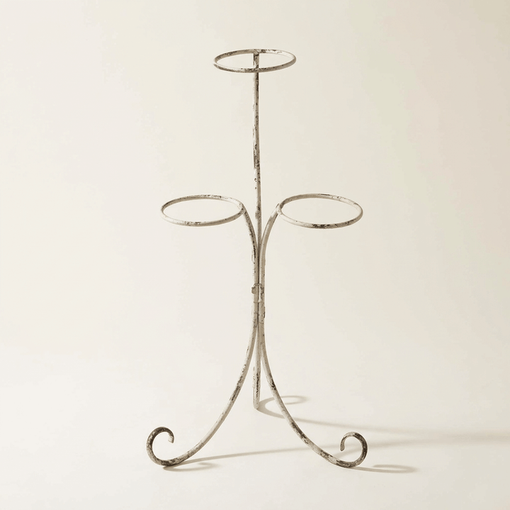 Antiqued ivory iron three-pot plant stand with open circular holders and curled feet on a neutral studio background.