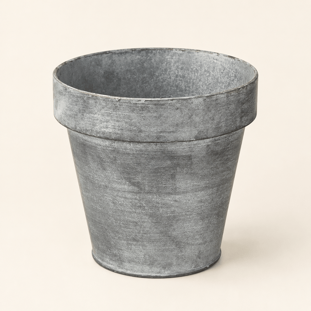 Empty zinc-finish metal planter with a tapered shape and broad rim against an ivory background.