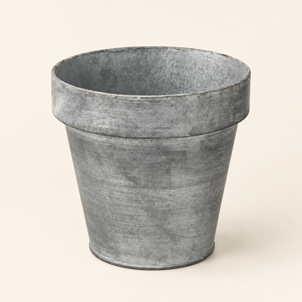 Empty zinc-finish metal planter with a tapered shape and broad rim against an ivory background.