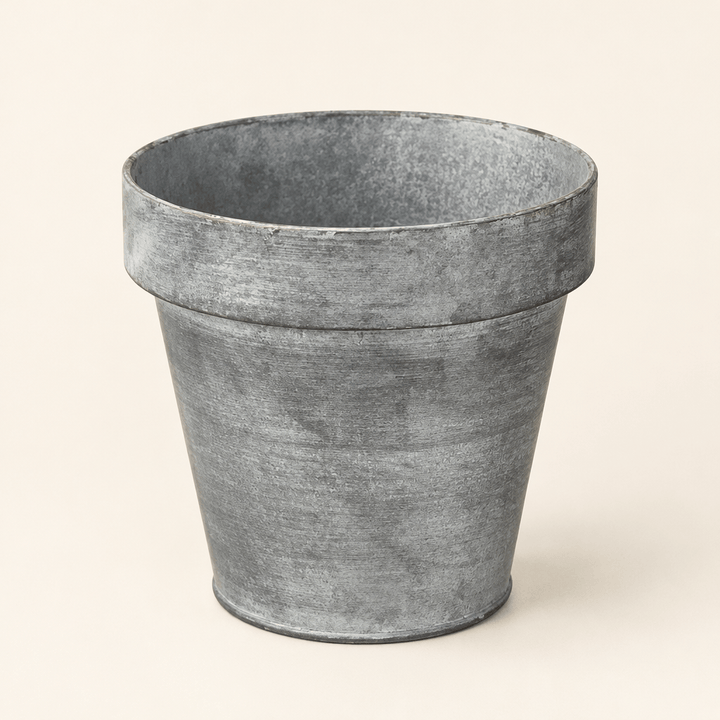 Empty zinc-finish metal planter with a tapered shape and broad rim against an ivory background.