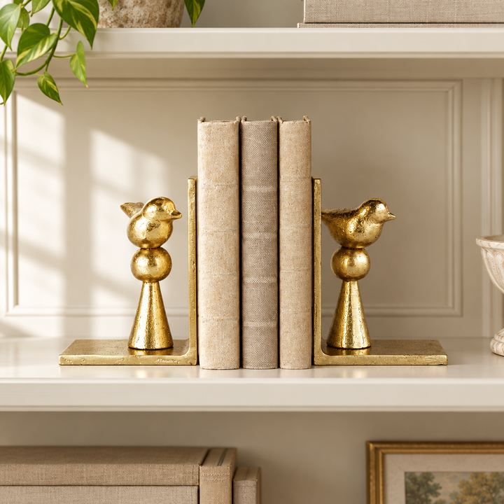 Gold aluminum songbird bookend pair styled with books on a cream library shelf.