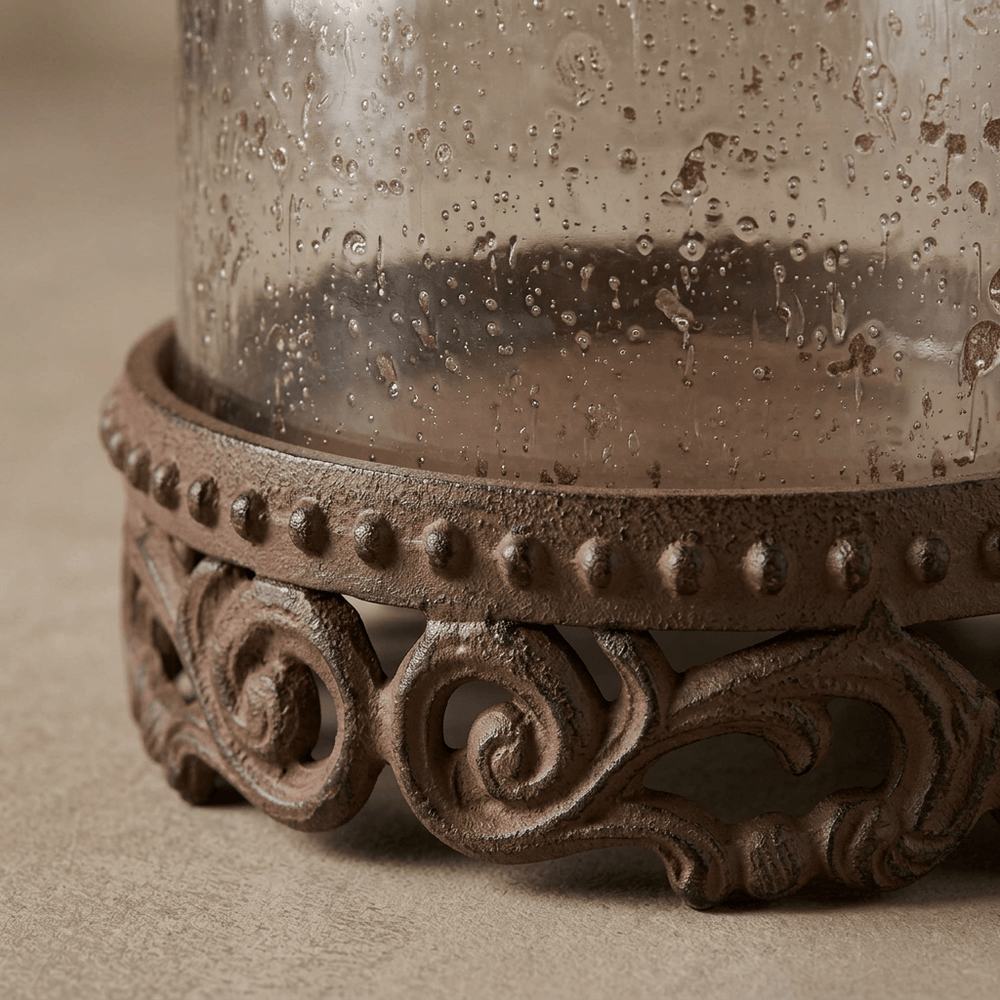 Close-up of Bellavita hurricane candle holder showing textured glass, beaded edging, and brown acanthus-leaf metalwork.