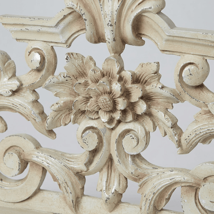 Close-up of the dimensional central flower and scrolling filigree on the antique-white mantel sculpture.