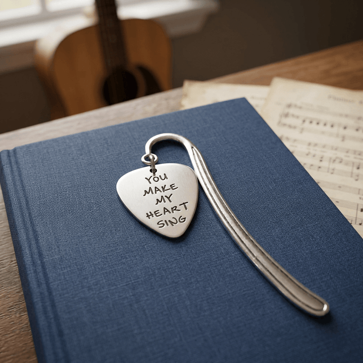 Metal guitar-pick bookmark on a clothbound book with a guitar in the background.