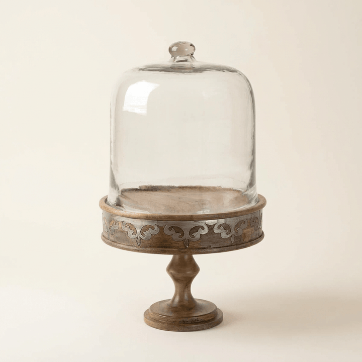Belvedere Cake Pedestal with Glass Dome showing warm mango wood and silver-tone scrollwork on ivory.