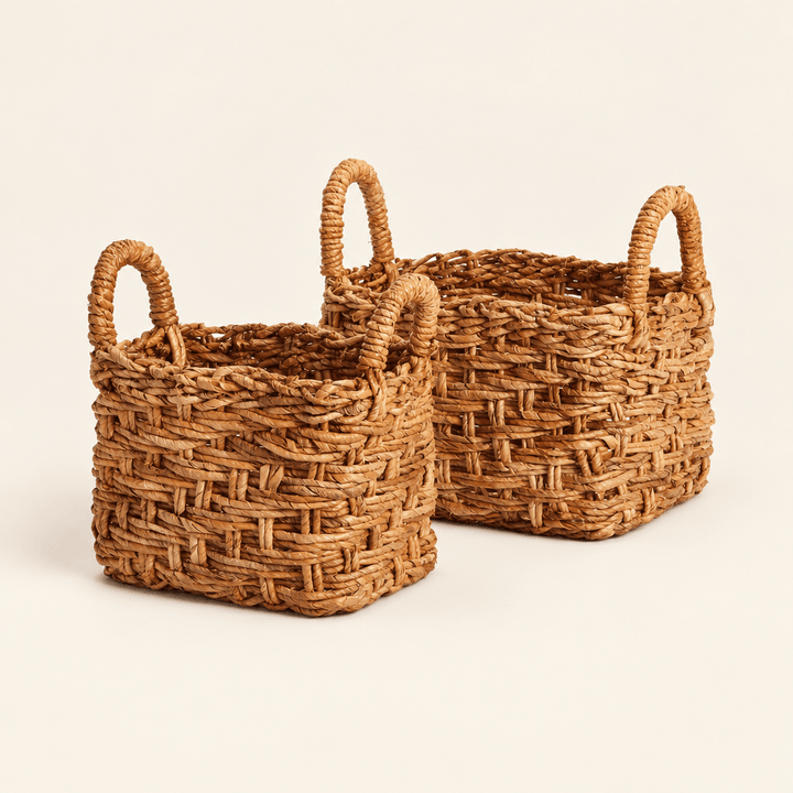 Two natural braided banana leaf baskets with loop handles on an ivory studio background