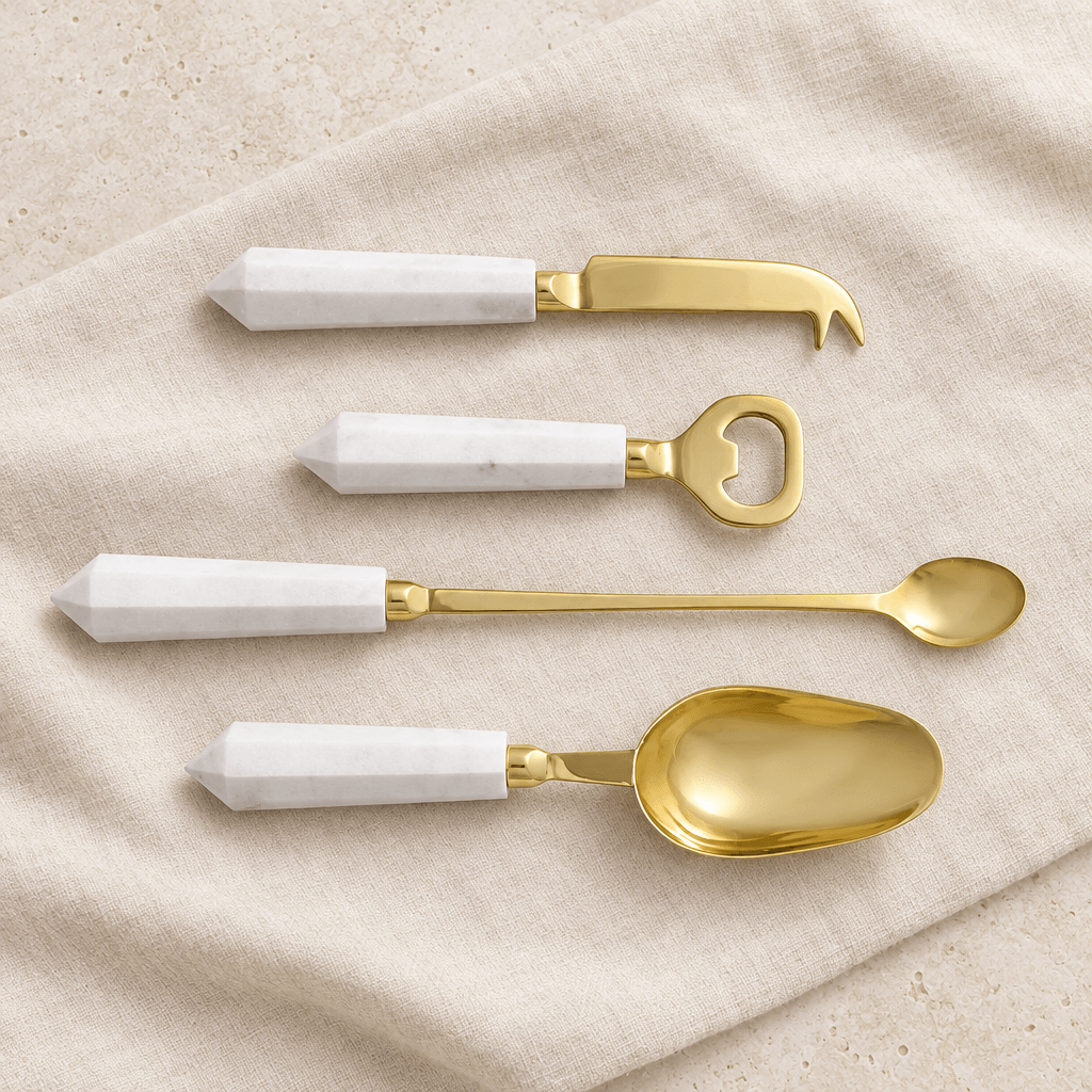 Four white marble and gold cocktail tools arranged on ivory linen.