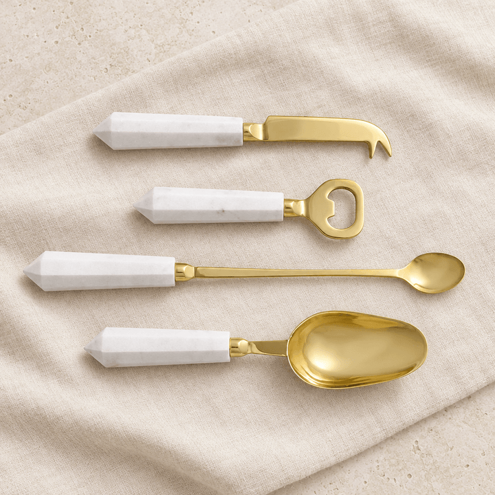 Four white marble and gold cocktail tools arranged on ivory linen.