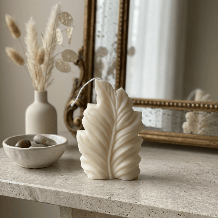 Ivory feather-shaped soy wax candle styled on a pale stone console with ceramics and dried stems.