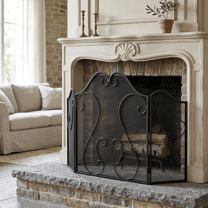 Black scrollwork fireplace screen standing on a stone hearth before a classic pale mantel