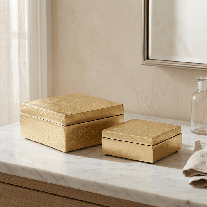 Pair of gold lidded aluminum storage boxes styled on a pale marble vanity.