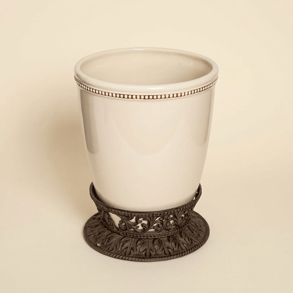 Bellavita cream stoneware wastebasket with ornate dark brown metal pedestal on an ivory studio background