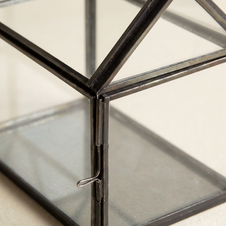 Close-up of the black iron frame, glass roof panels, and side door latch of the miniature greenhouse terrarium.