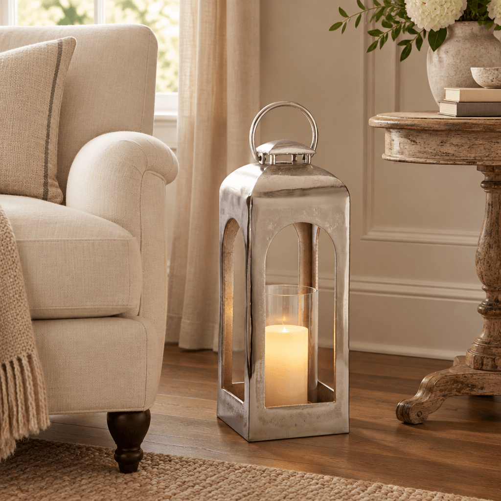 Silver aluminum lantern with a glowing flameless candle beside a cream linen armchair indoors