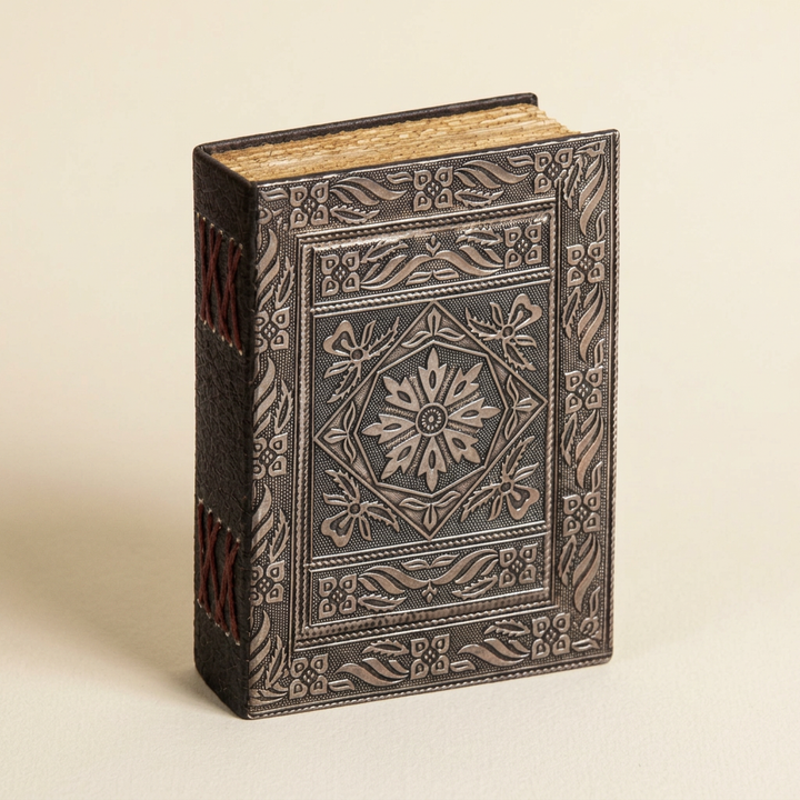 Silver floral embossed leather journal with dark leather spine and red stitching on an ivory background