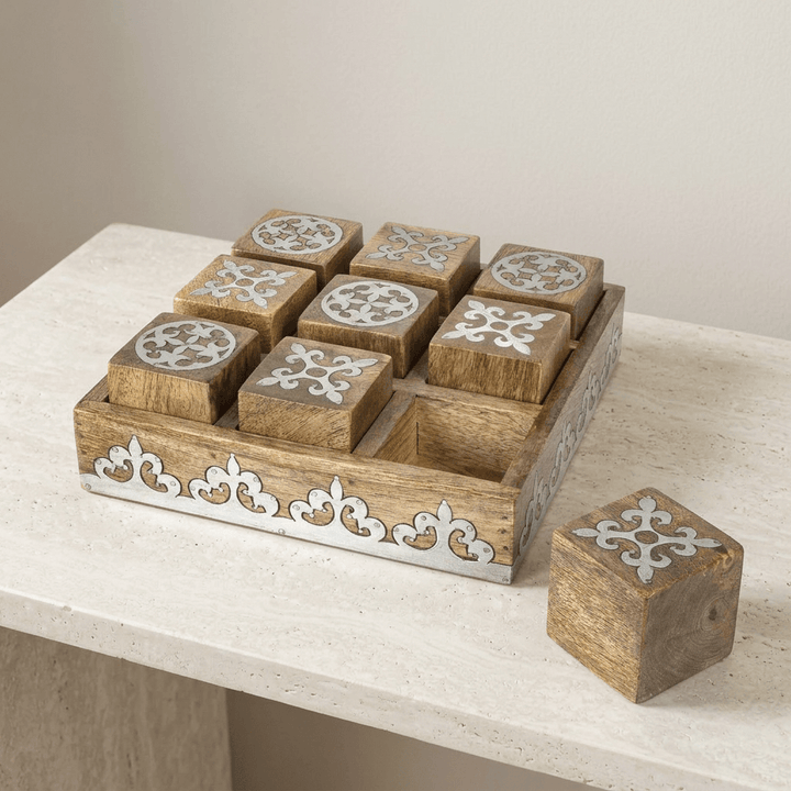 Belvedere mango wood tic tac toe board and decorative metal-inlaid playing cubes on a pale stone console.