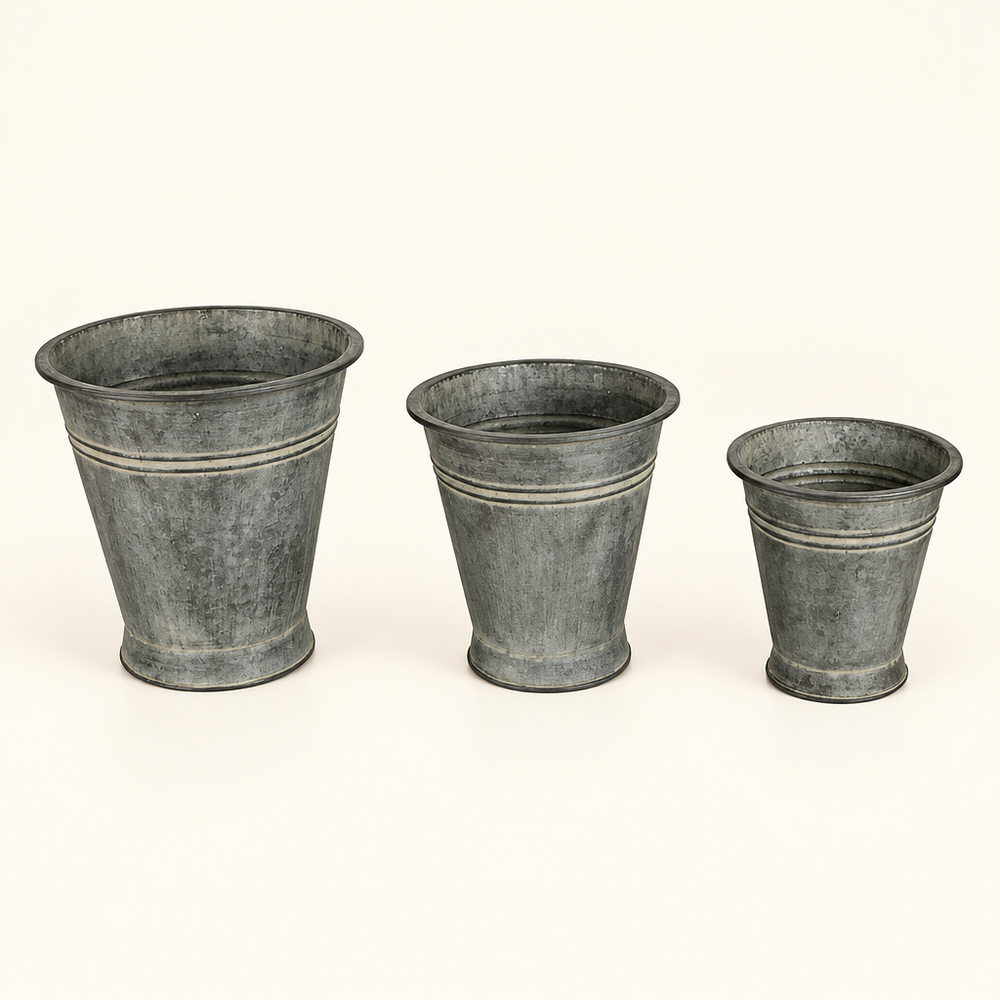Three graduated metal bucket planters with tapered shapes and an aged finish on ivory.