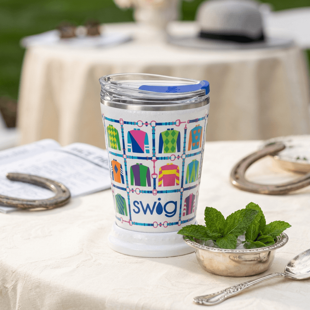 Jockey-silk mint julep tumbler on a cream linen Derby table beside fresh mint and a silver serving spoon.