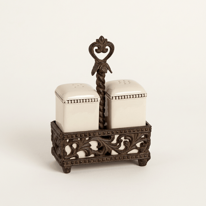 Bellavita cream ceramic salt and pepper shakers in an ornate brown metal holder on a warm white background.