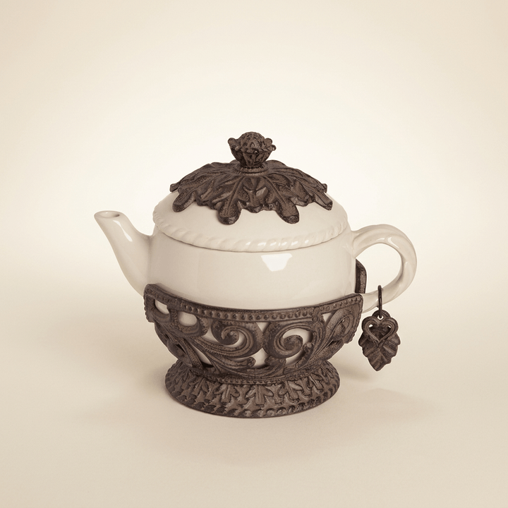 Cream teapot in ornate dark brown metal cradle with leaf detailing on an ivory background