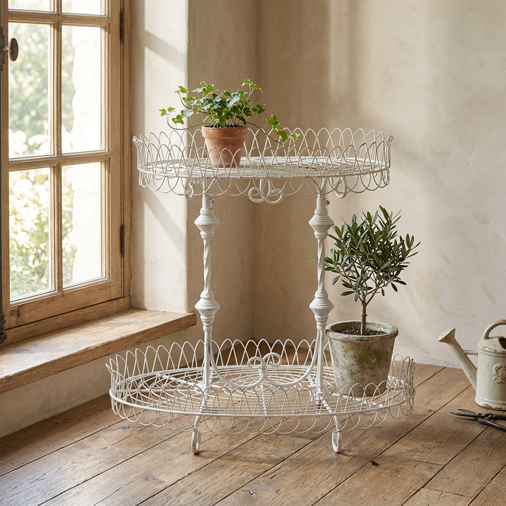 Fleury antiqued white two-tier iron plant stand styled with potted greenery beside a sunny window.