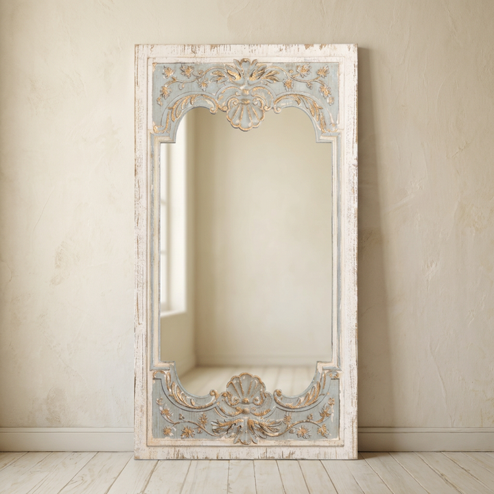 Avelune Carved Wood Mirror with distressed ivory and pale blue frame and ornate shell details against a warm neutral wall.