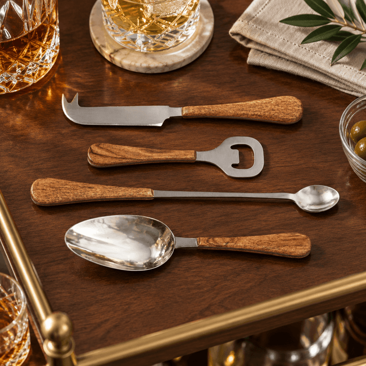 Acacia wood handled stainless steel cocktail accessories arranged on a walnut bar cart.
