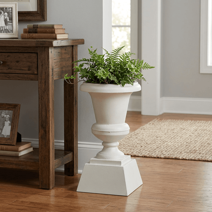 Hawthorne Aged Iron Urn Planter in Soft White, styled with greenery on the floor beside a wooden entry console.