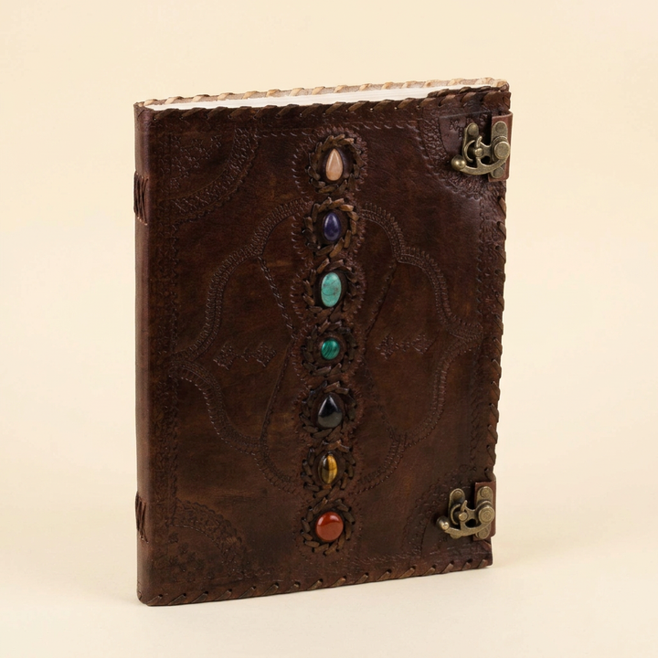 Brown embossed leather journal with seven colorful stones and two metal clasps on an ivory background